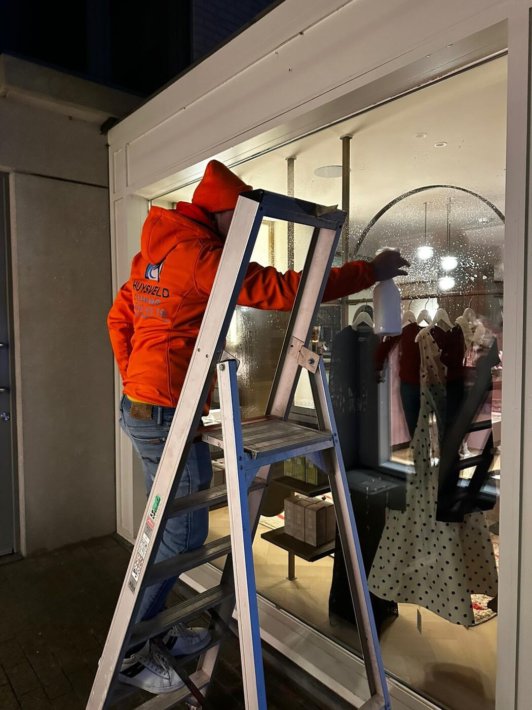 Tom op een ladder bij een winkeletalage in de avond